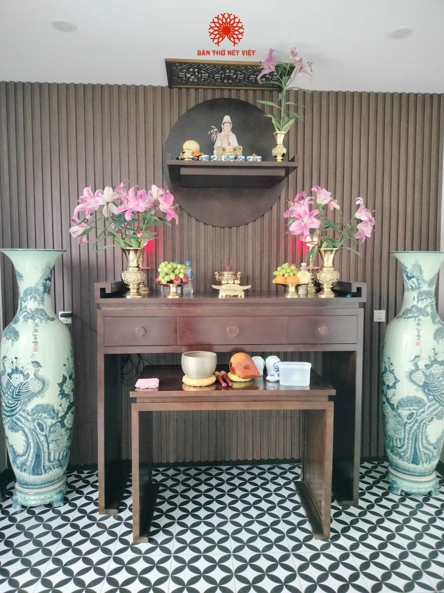 Đa phần không gian phòng thờ luôn được các quý gia chủ rất quan tâm và chú trọng rất nhiều, đặc biệt là về phần chất lượng sản phẩm và không gian yêu cầu phải đạt tính thẩm mỹ, sang trọng và trang nghiêm. Chính vì những điều đó, Bàn Thờ Nét Việt không ngừng cập nhật những mẫu phòng thờ đẹp và đặc trưng với chất liệu gỗ tự nhiên chọn lọc cùng hương thơm nhẹ nhàng, mang lại nét kiến trúc đẳng cấp cho chốn tâm linh.Chất liệu gỗ tự nhiên cao cấp và đa dạng theo nhu cầu gia chủSản phẩm hiện trạng sẵn có được chế tác từ 100% gỗ sồi tự nhiên nhập khẩu. Gỗ sồi sở hữu chất gỗ cứng cáp, chịu lực cực tốt, vân gỗ elip hiện đại và lên màu sơn vô cùng sắc nét. Để mang lại sự linh hoạt và đáp ứng trọn vẹn mong muốn của từng gia đình, Bàn Thờ Nét Việt còn cung cấp dịch vụ đặt đóng sản phẩm bằng các chất liệu gỗ tâm linh cao cấp khác theo nhu cầu riêng của gia chủ:Gỗ Gụ: Đầm chắc, thớ mịn, mang sắc vị cổ kính và trang nghiêm truyền đời.Gỗ Mít: Sở hữu sắc vàng tâm linh trang nhã, mùi thơm nhẹ, mang ý nghĩa đón nhận bình an, đại cát.Gỗ Hương: Dòng gỗ quý hiếm thuộc nhóm I với hệ vân độc bản siêu đẹp và hương thơm tự nhiên thư thái.Toàn bộ phôi gỗ dù là gỗ sồi, gỗ gụ, gỗ hương hay gỗ mít đều trải qua quy trình tẩm sấy nghiêm ngặt, cam kết không pha tạp gỗ ép, giúp chống mối mọt và hạn chế tối đa tình trạng cong vênh theo thời gian.Thiết kế vách ốp và hệ thống bàn thờ thông minhSự kết hợp giữa mẫu bàn thờ đứng hiện đại và bàn thờ phụ (bàn cơm) độc lập di động phía dưới giúp tối ưu hóa công năng sử dụng. Bàn chính được thiết kế thêm các hộc chứa thông minh giúp gia chủ thuận tiện đựng các vật dụng đồ cúng như nhang, nến, bật lửa. Bàn thờ phụ hỗ trợ đắc lực cho bạn trong việc bày trí mâm cơm cúng vào các dịp đại lễ, dễ dàng phân chia rõ ràng giữa món mặn hay món chay. Nếu diện tích phòng của gia đình hạn chế, bạn cũng có thể tham khảo thêm các giải pháp từ dòng bàn thờ treo tường thông minh của chúng tôi để tối ưu không gian nền.Hệ thống vách ốp hậu trang trí phía sau ban thờ với những đường cắt CNC chính xác, vuông vắn tạo nên một diện mạo hoàn hảo giúp cho không gian phòng thờ trở nên bề thế và đẳng cấp hơn bao giờ hết. Sự hòa quyện giữa các đường vân gỗ tự nhiên và ánh sáng vàng phát hào quang mang lại hiệu ứng thị giác tráng lệ, ấm cúng, giúp xua tan tà khí và tụ hội vượng khí cho ngôi nhà.